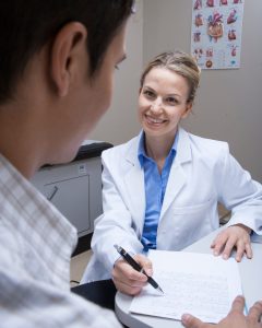 An image of a female physician and a male patient looking down at a medical report in an office setting.