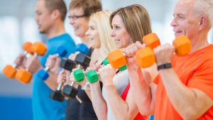 Image displays a group of men and women in a workout setting and clothing, lifting weights.
